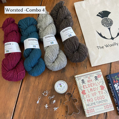 The Swedish Book Bundle components which include two books by Helene Tursten, TWT Tote bag, Stitch marker set, gingerbread cookie cutter, and Ullcentrum Worsted Weight yarn. Components are shown and laid out on table. Colors in worsted combo 4 include a red, blue, grey, and brown. 