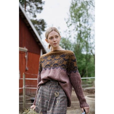 Model standing outside barn wearing Pohjolan Neito Sweater knit with Tukuwool DK in colors Ujo, Nila, and Tynni with a colorwork yoke.
