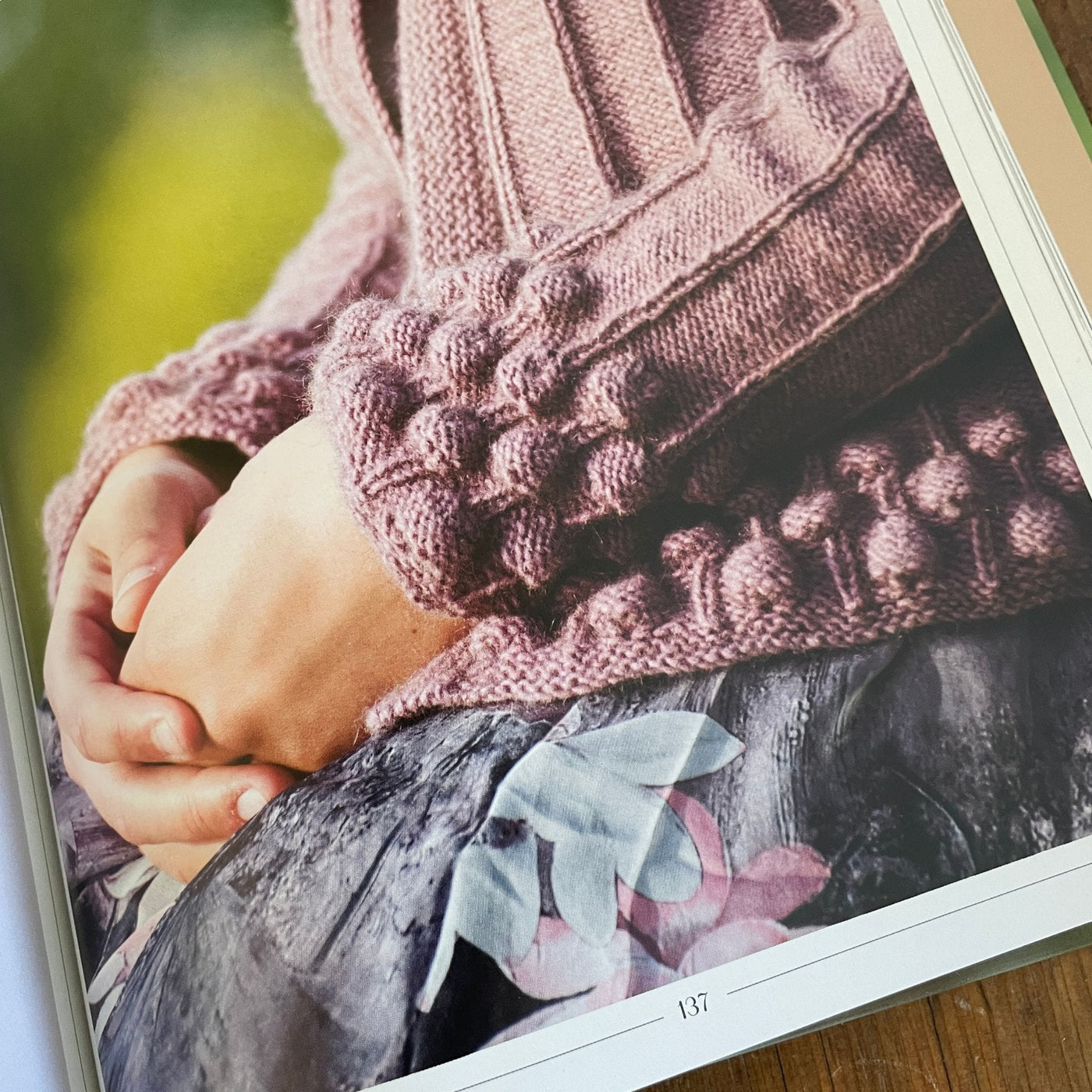 Inside pages of book Norwegian Sweaters & Jackets by Kari Hestnes shows close up of pattern detail texture and bauble on cuffs and hem of mauve sweater.