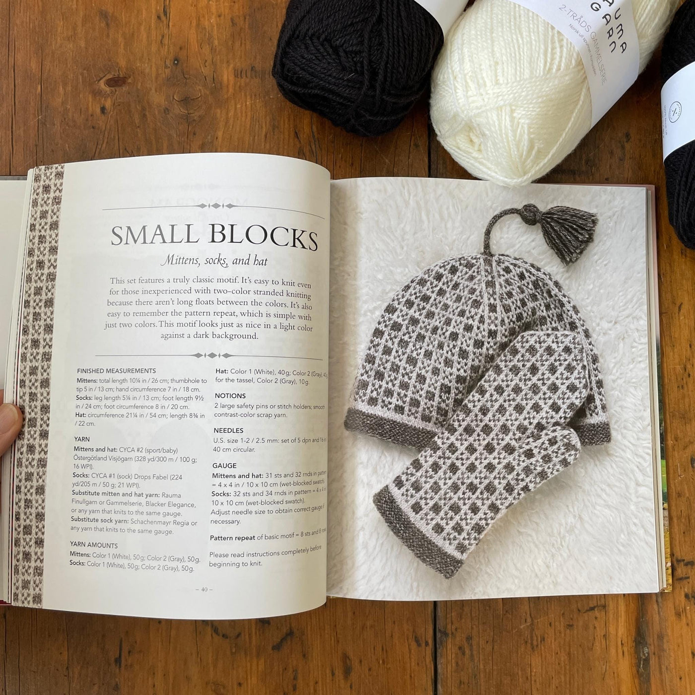 Page of Traditional Nordic Knits book with black and white colorwork mittens and hat with yarn beside book.