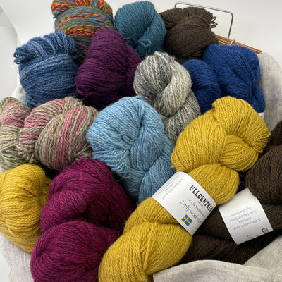 Many colors of Ullcentrum Sport Weight Yarn in skeins arranged in basket with yellow skein turned sideways so label can be seen..