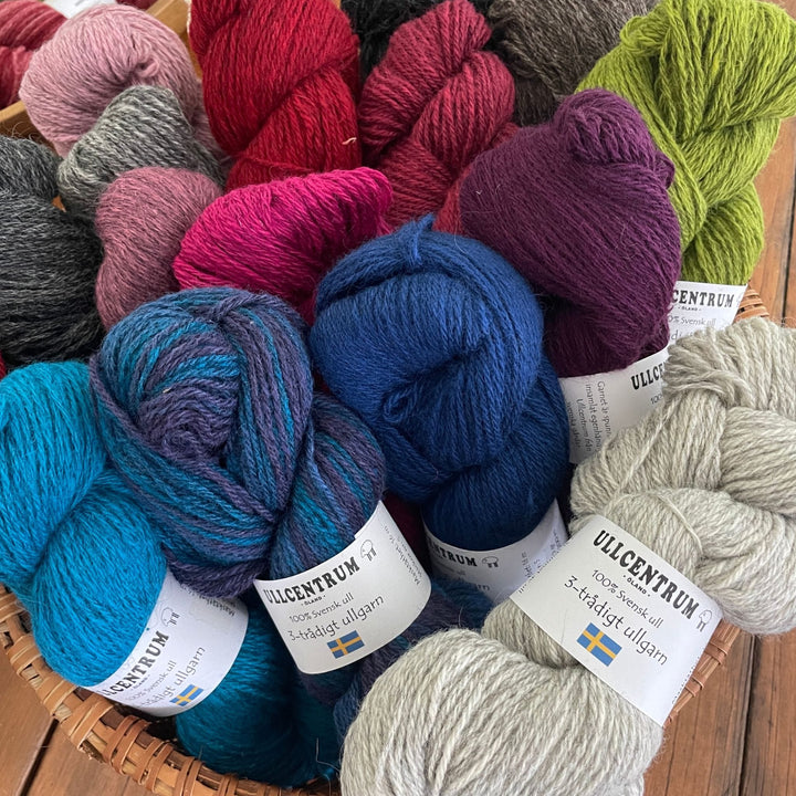 Many skeins of Ullcentrum 3-ply, a worsted weight yarn, in several colors, including blues, reds, greys, purple, and green