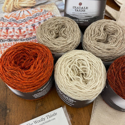 Components of the Bonnie Isle Hat Yarn Set using 6 cakes of Uradale 2ply Jumper Weight Yarn in Neutrals and two shades of orange. Yarn is shown up close with a stitch marker, The Woolly Thistle tote bag and a photo of the finished Bonnie Isle Hat partially in view..