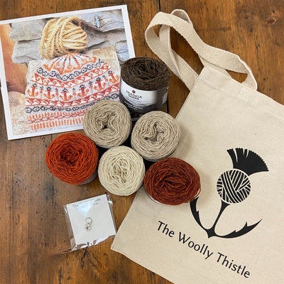 Components of the Bonnie Isle Hat Yarn Set using 6 cakes of Uradale 2ply Jumper Weight Yarn in Neutrals and two shades of orange. Yarn is shown with a stitch marker, The Woolly Thistle tote bag and a photo of the finished Bonnie Isle Hat.