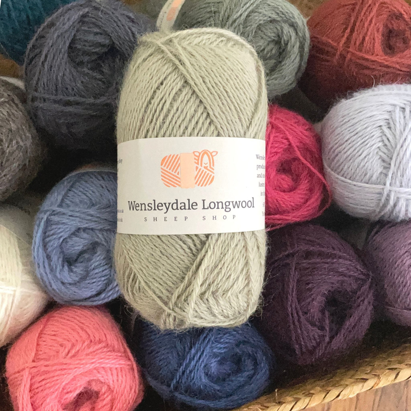 A pile of 50 gram balls of Wensleydale Longwool Sheep Shop 4ply yarn, a fingering weight yarn, in a variety of colors with a light sage green ball on top