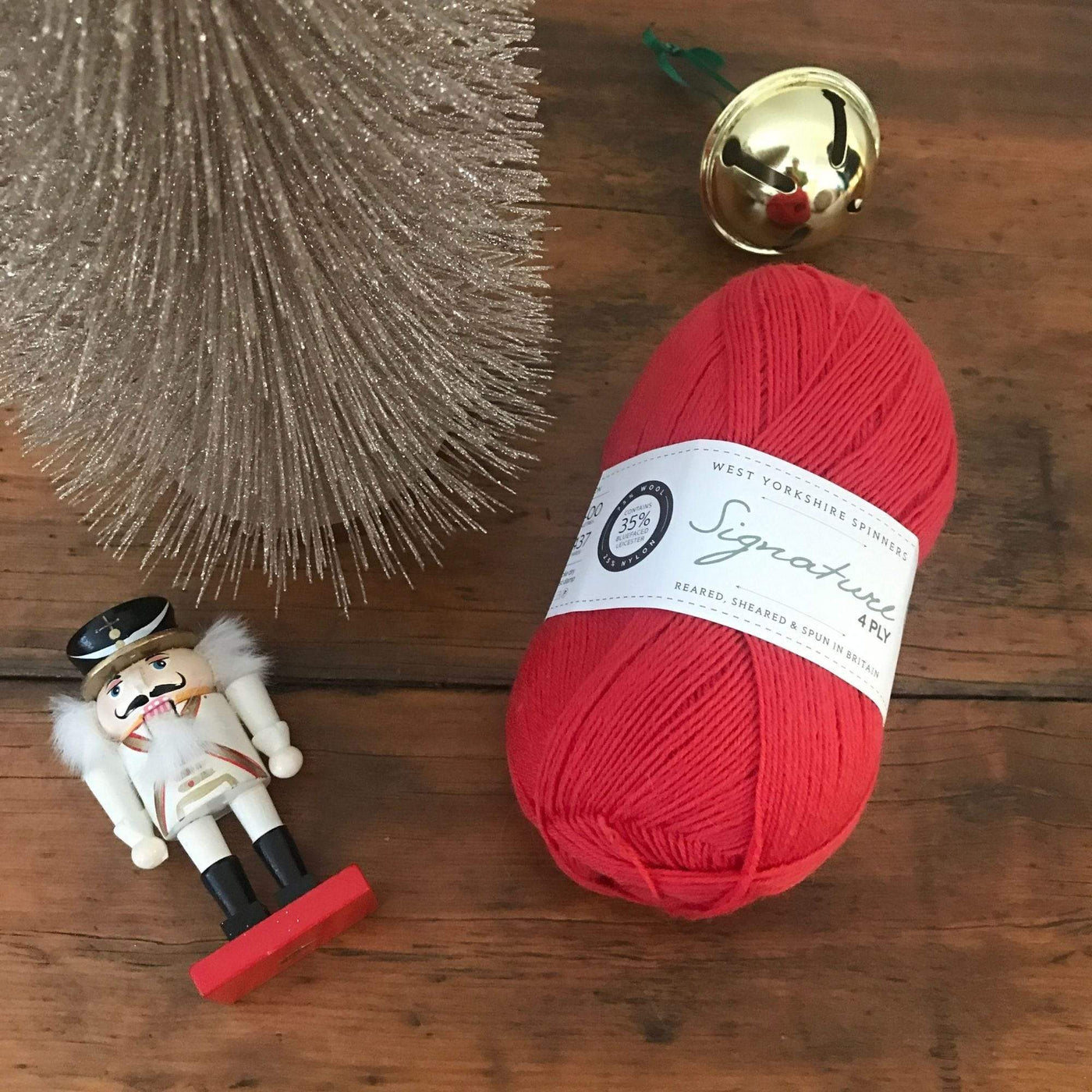 A ball of West Yorkshire Spinners Signature 4ply yarn, fingering weight, on a wood table with Christmas decorations